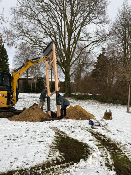 Weert_Paalkast_Vleermuis_Plaatsing In afbeelding van twee mannen en een graafmachine die een paalkast c.q. kraamkast voor vleermuizen plaatsen in de sneeuw ergens in een park in de gemeente Weert.